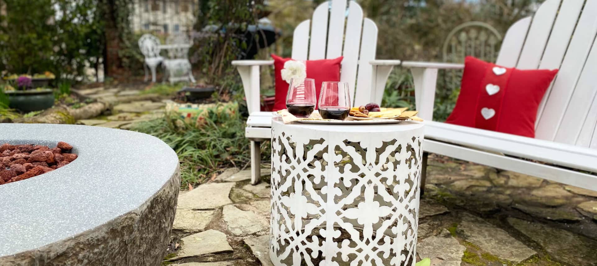 Wine and cheese tray in garden near white chairs and fire pit