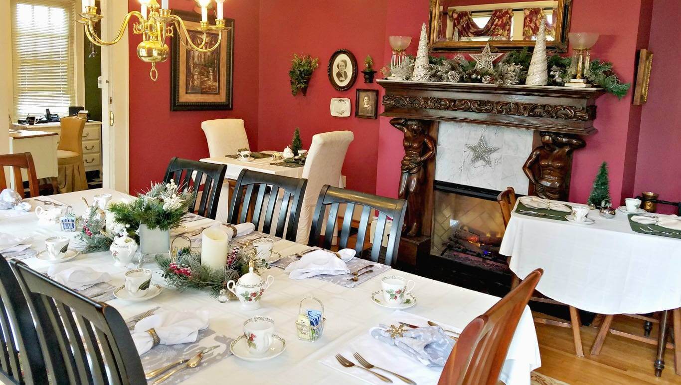 Long dining room table set to serve eight in winter whites and silver in front of carved wooden mantle.